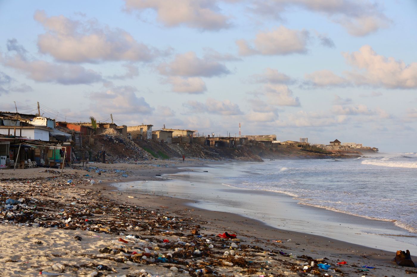 Discarded second-hand clothing and worn footwear piled on a coastal beach