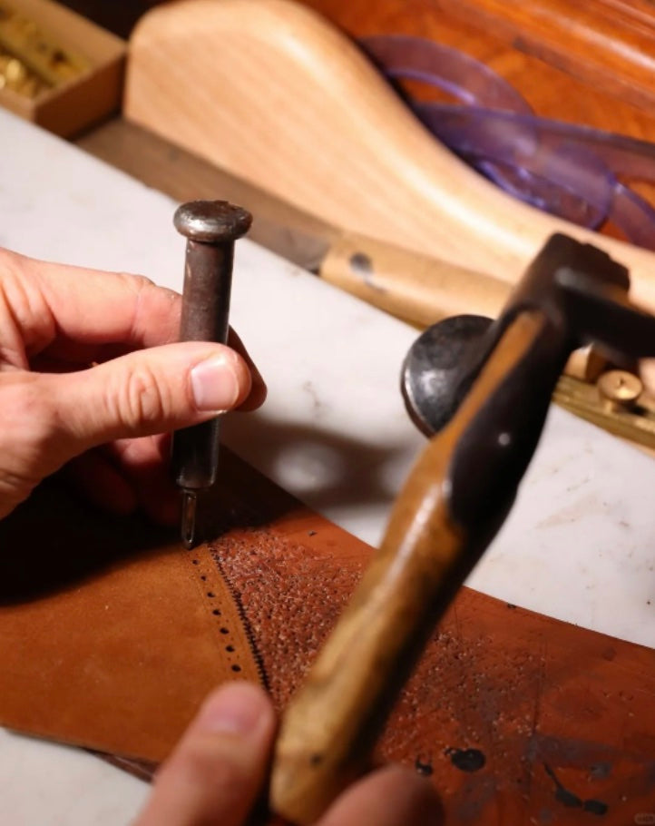 Artisan punching decorative holes into leather with a hammer and awl