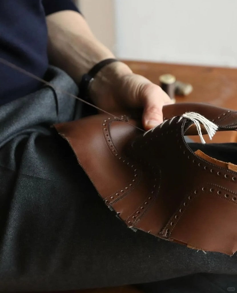 Close-up of a craftsman hand-stitching a premium brown leather brogue shoe in the HAJINK workshop